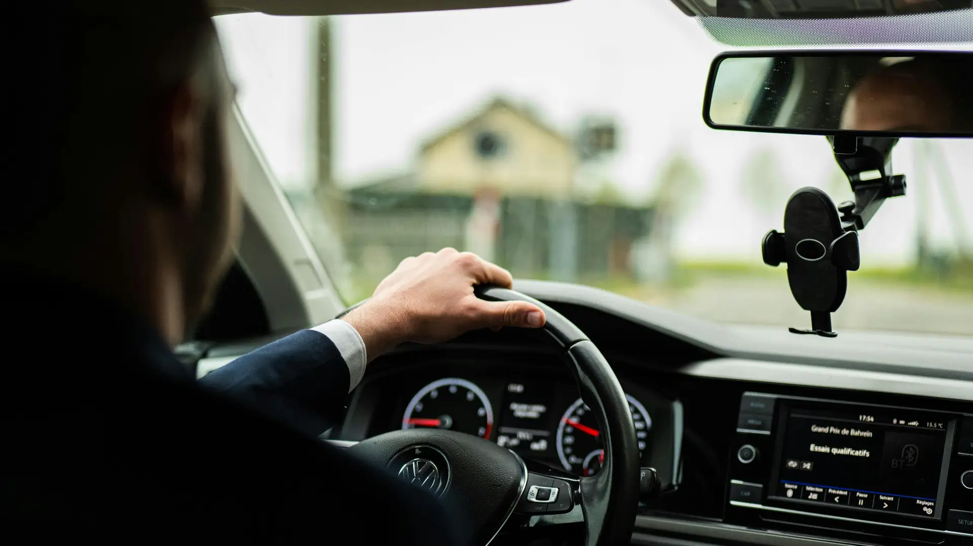 Businessman in suit driving a car, focus on steering wheel and dashboard.