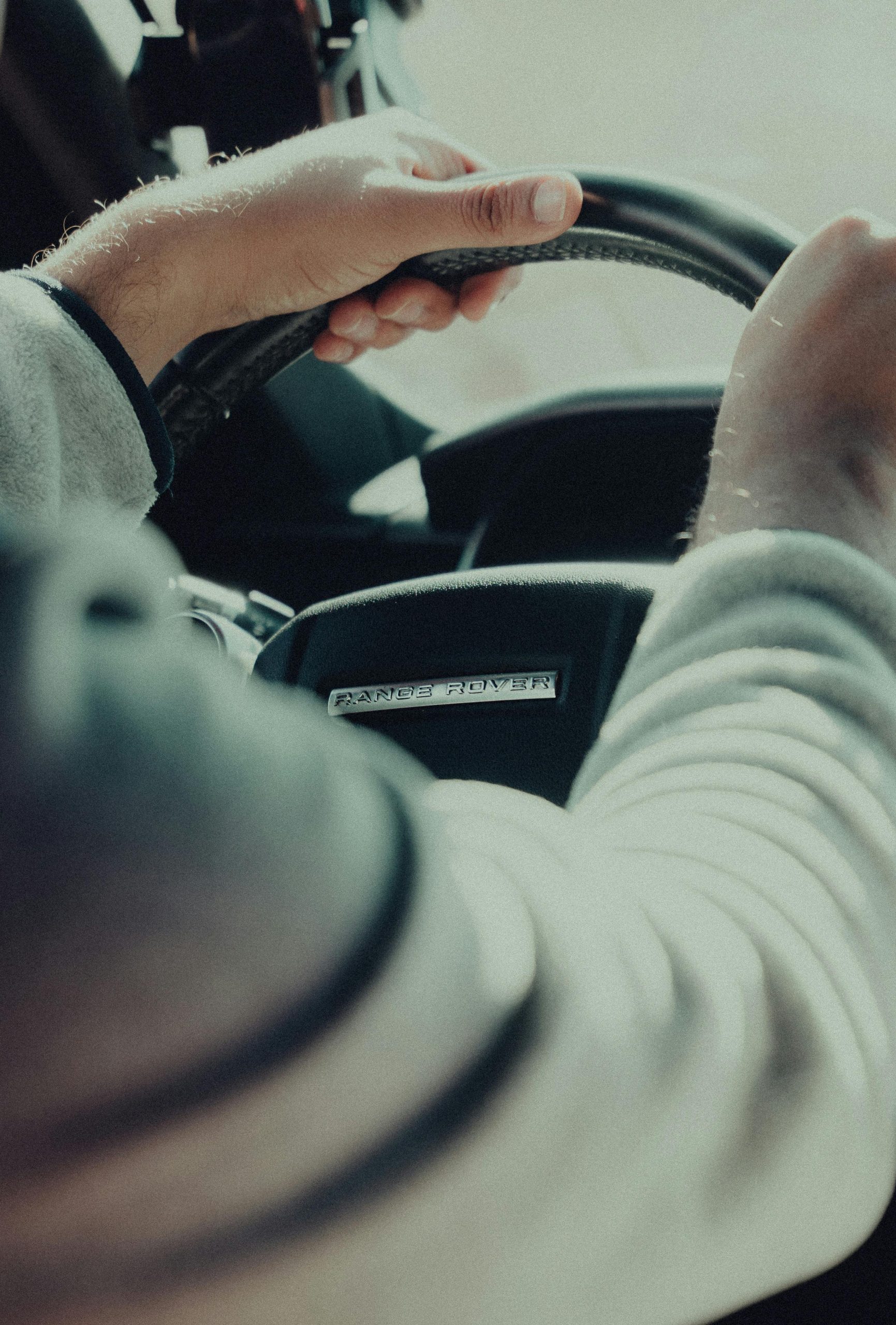 Hands on steering wheel of a Range Rover, showcasing driving focus and control.